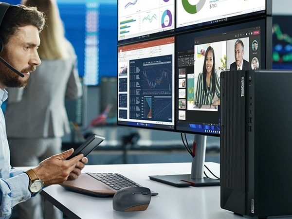 Ein Mann mit Headset und Telefon blickt auf einen Lenovo ThinkCentre M90t Gen 4 Tower-PC auf einem Schreibtisch mit vier Monitoren und einer kabellosen Tastatur und Maus