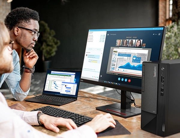 Zwei Personen an einem Schreibtisch mit einem ThinkCentre Neo 50t Gen 4 (Intel) Business-Tower mit optionalem Monitor und Smart Cable