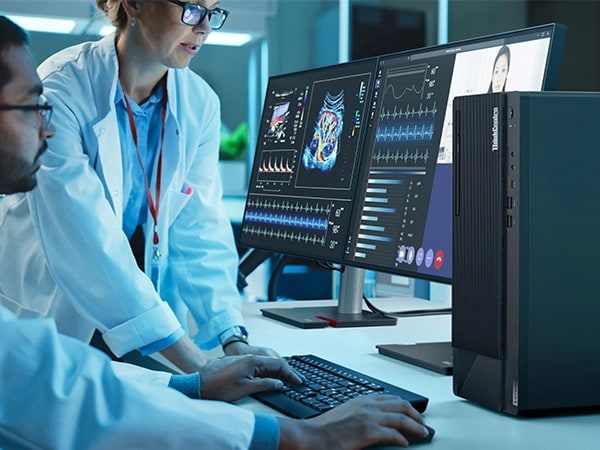 Ein Mann und eine Frau in Laborkitteln verwenden einen Lenovo ThinkCentre M90t Gen 4 Tower-PC mit zwei Monitoren und einer kabellosen Tastatur- und Maus-Kombination